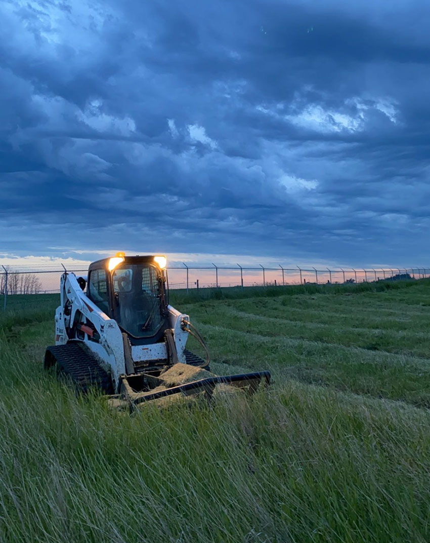 A tractor stands prominently in the center of a vast, open field, surrounded by greenery and agricultural land.