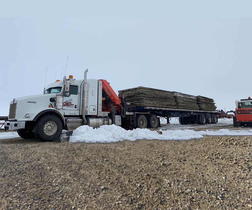 A large truck transporting logs on a snowy road, surrounded by a winter landscape.