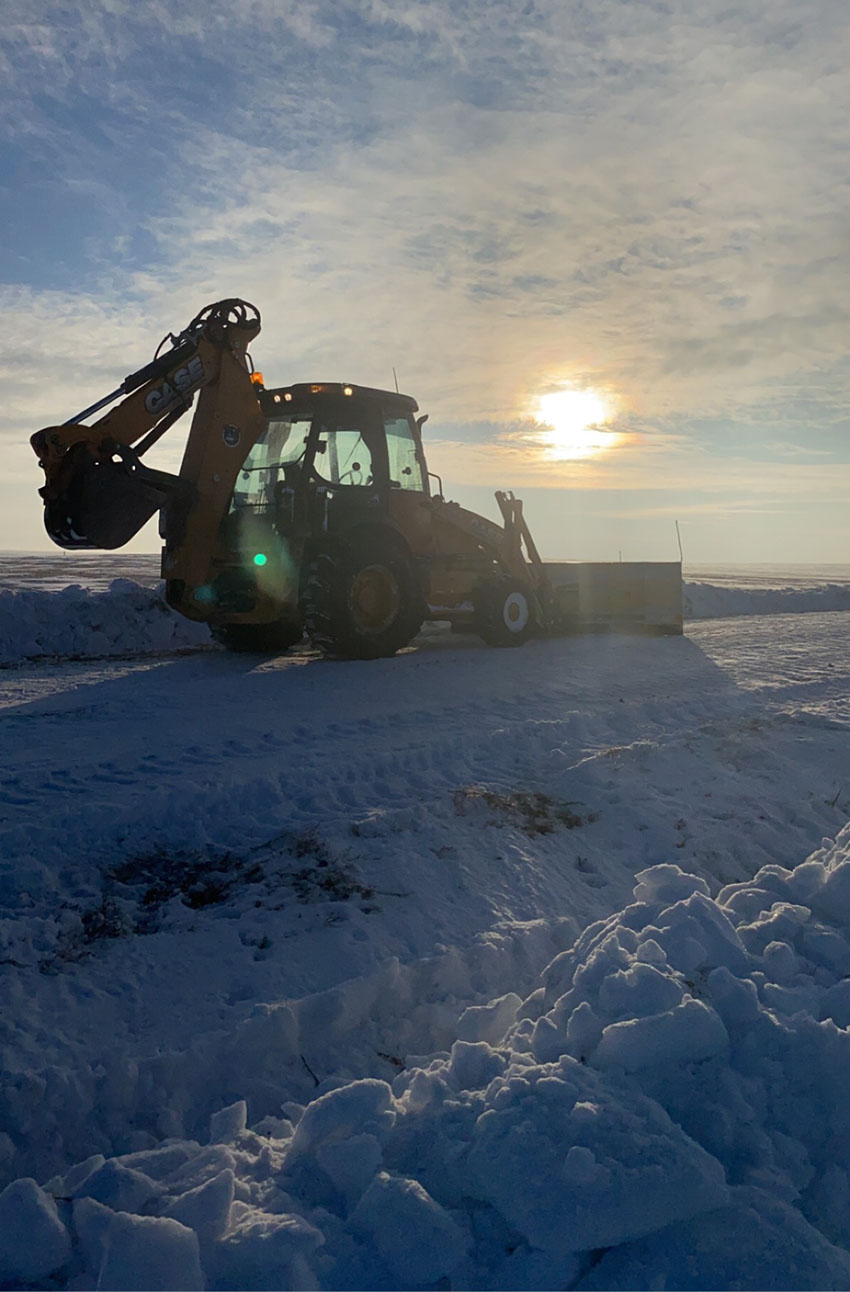 A bulldozer clears snow from a road, showcasing its powerful machinery against a winter landscape.