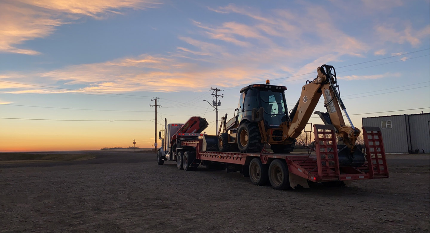 A truck transporting a backhoe, showcasing heavy machinery for construction or excavation purposes.