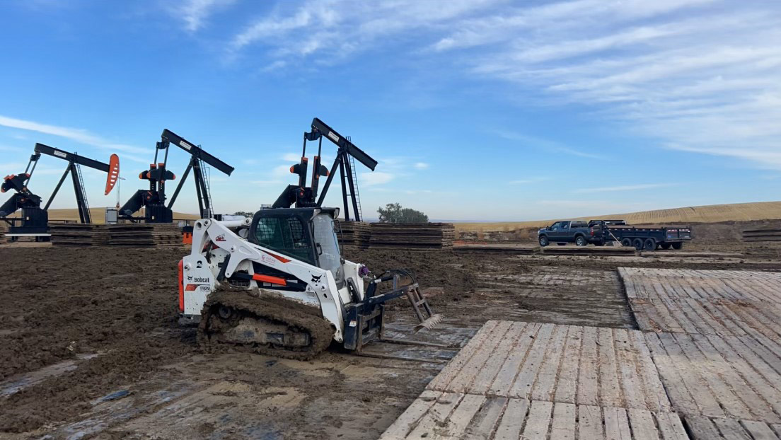 A construction crew is actively working on a dirt road, using machinery and tools to improve the surface.