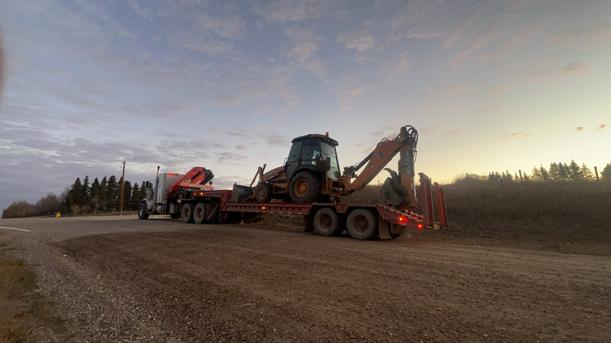 A large truck transporting a tractor along a rugged dirt road, showcasing the vehicle's power and utility in rural settings.
