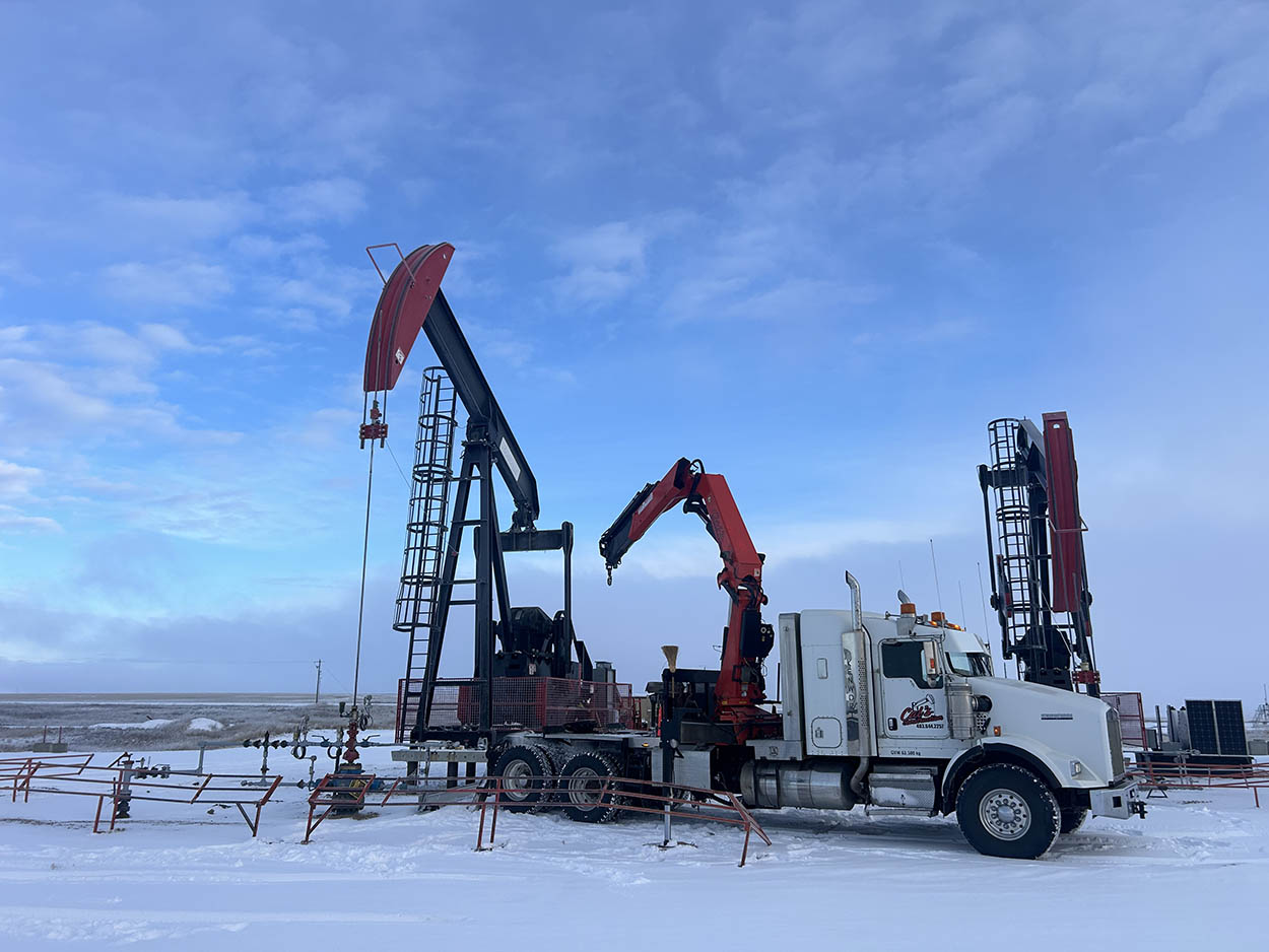 A truck with a large oil pump in the snow, accompanied by two additional trucks loaded with equipment.